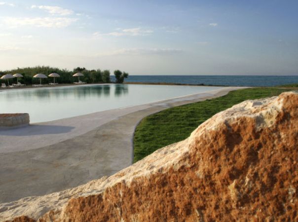 Piscina all'aperto con vista mare e ombrelloni in lontananza.