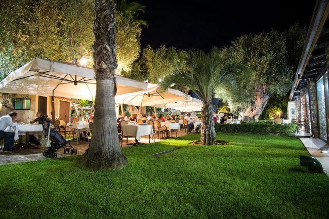 Giardino di un ristorante con tavoli illuminati e palme.