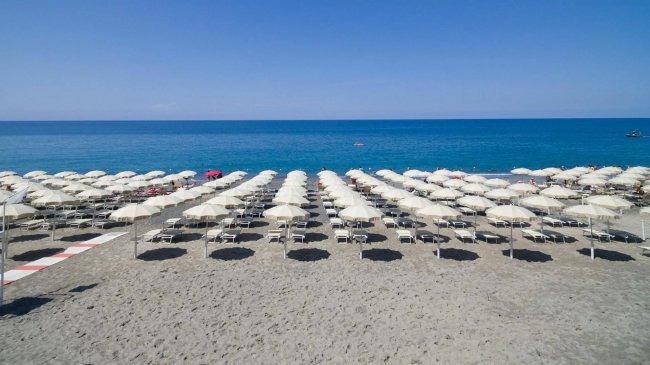 Spiaggia con file di ombrelloni bianchi e mare blu.