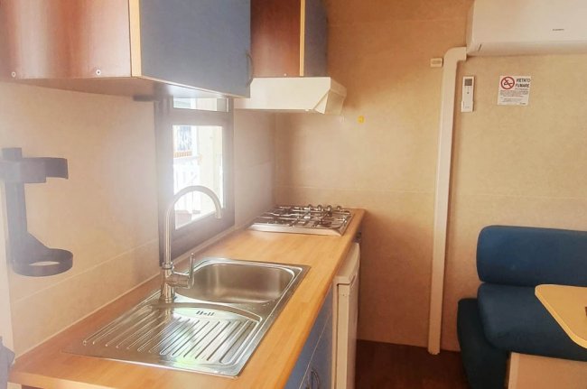 Cucina compatta con lavello, fornello, e mobili blu, all'interno di una casa mobile.