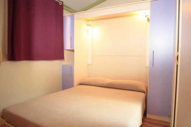Letto matrimoniale sotto luce calda, tende viola.