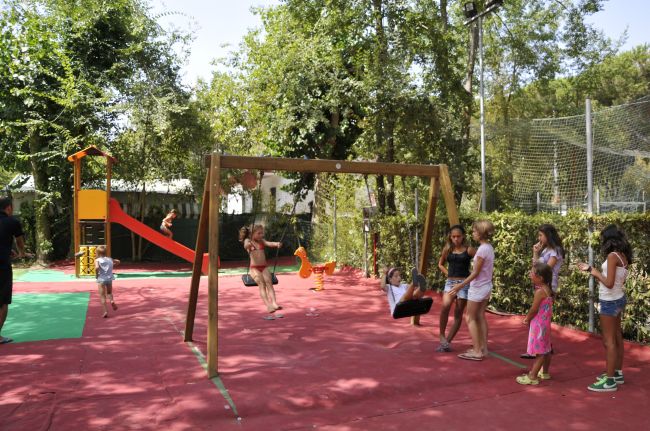 Parco giochi con scivolo, altalene e bambini che giocano.