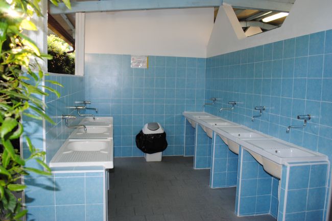 Lavandini e doccia in un bagno pubblico con piastrelle blu.