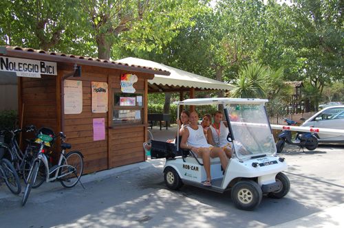 Un golf cart con quattro persone sedute davanti a un chiosco di noleggio bici in un'area verde.