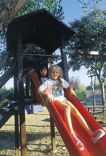 Due bambini scendono sorridenti da uno scivolo rosso al parco giochi.