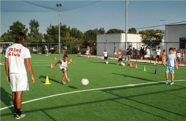 Bambino calcia un pallone in un campo da gioco all'aperto.