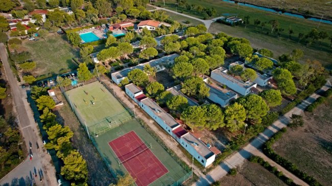 Vista aerea di un complesso con campi da tennis, piscine e edifici immersi nel verde.