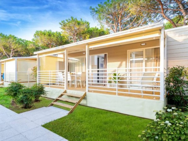 Una casa prefabbricata con terrazza, circondata da alberi e prato verde.