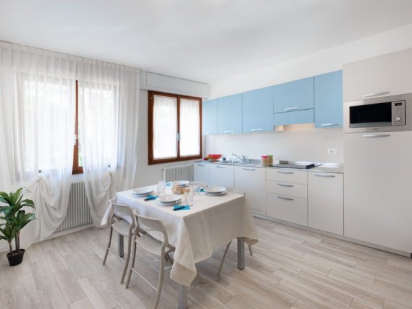 Cucina moderna con mobiletti azzurri, tavolo apparecchiato e finestre con tende bianche.