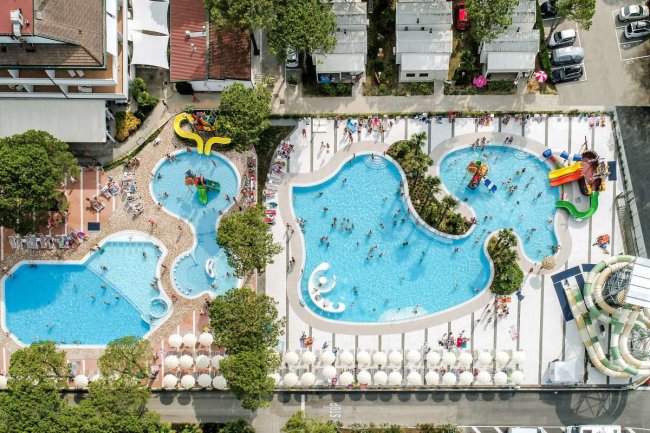 Immagine dall'alto di piscine con scivoli, lettini e ombrelloni, vista dettagliata del complesso.