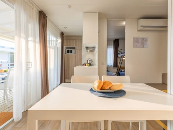 Tavolo bianco con pane, cucina moderna, aria condizionata, e uscita su patio soleggiato.