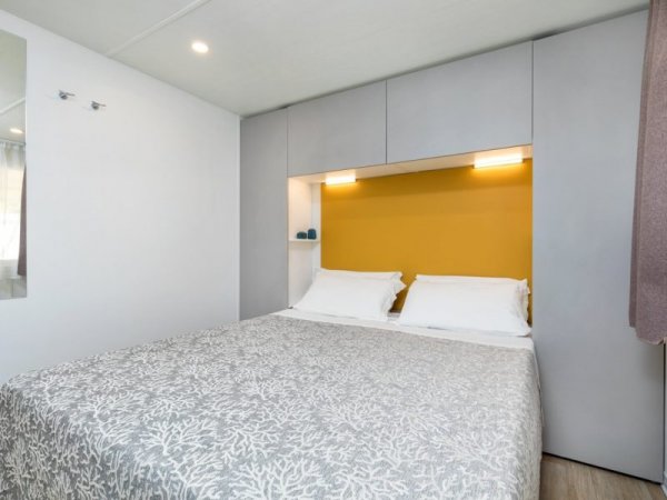 Letto matrimoniale con lenzuola bianche, parete gialla e armadi grigi.