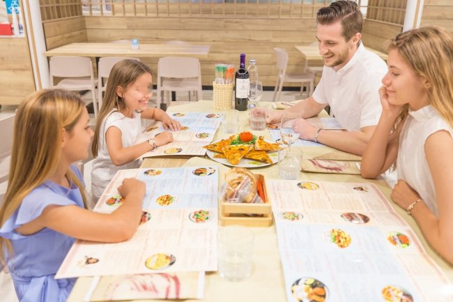 Famiglia seduta intorno a un tavolo al ristorante, sorridendo davanti a un piatto di pizza.