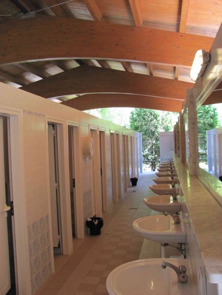 Interno di un bagno pubblico con lavandini e cabine, soffitto in legno arcuato.