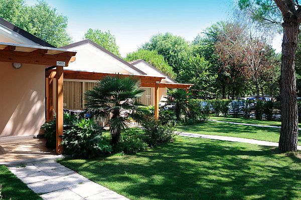 Un bungalow con terrazza coperta, circondato da prati e alberi.