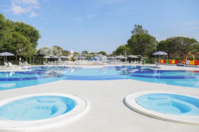 Una piscina con lettini e ombrelloni, due vasche idromassaggio in primo piano.