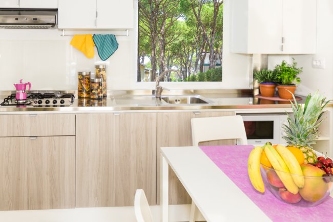 Cucina moderna con frutta sul tavolo e vista sul giardino alberato.